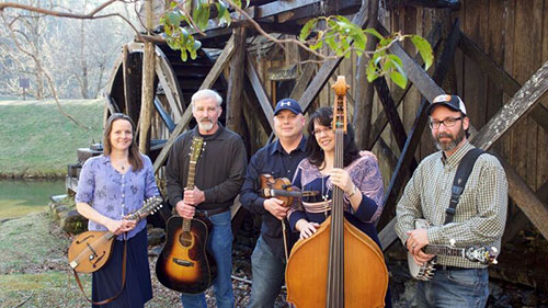 Five individuals posing and smiling while holding instruments and standing outside